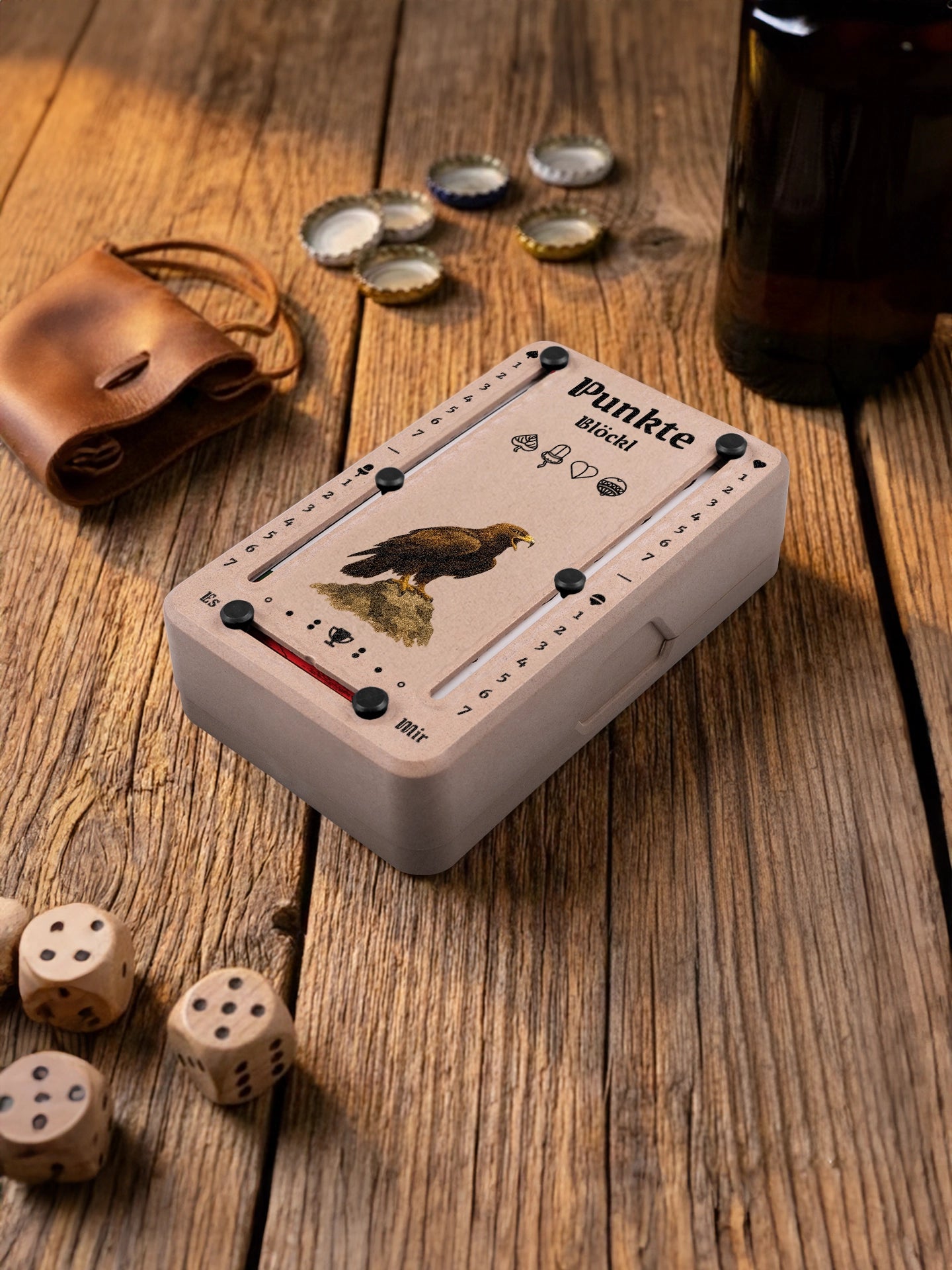 Punkteblöckl in Holzoptik mit schwarzen Pins und Adler-Motiv. Platziert auf Holztisch mit Würfeln und Kronkorken.