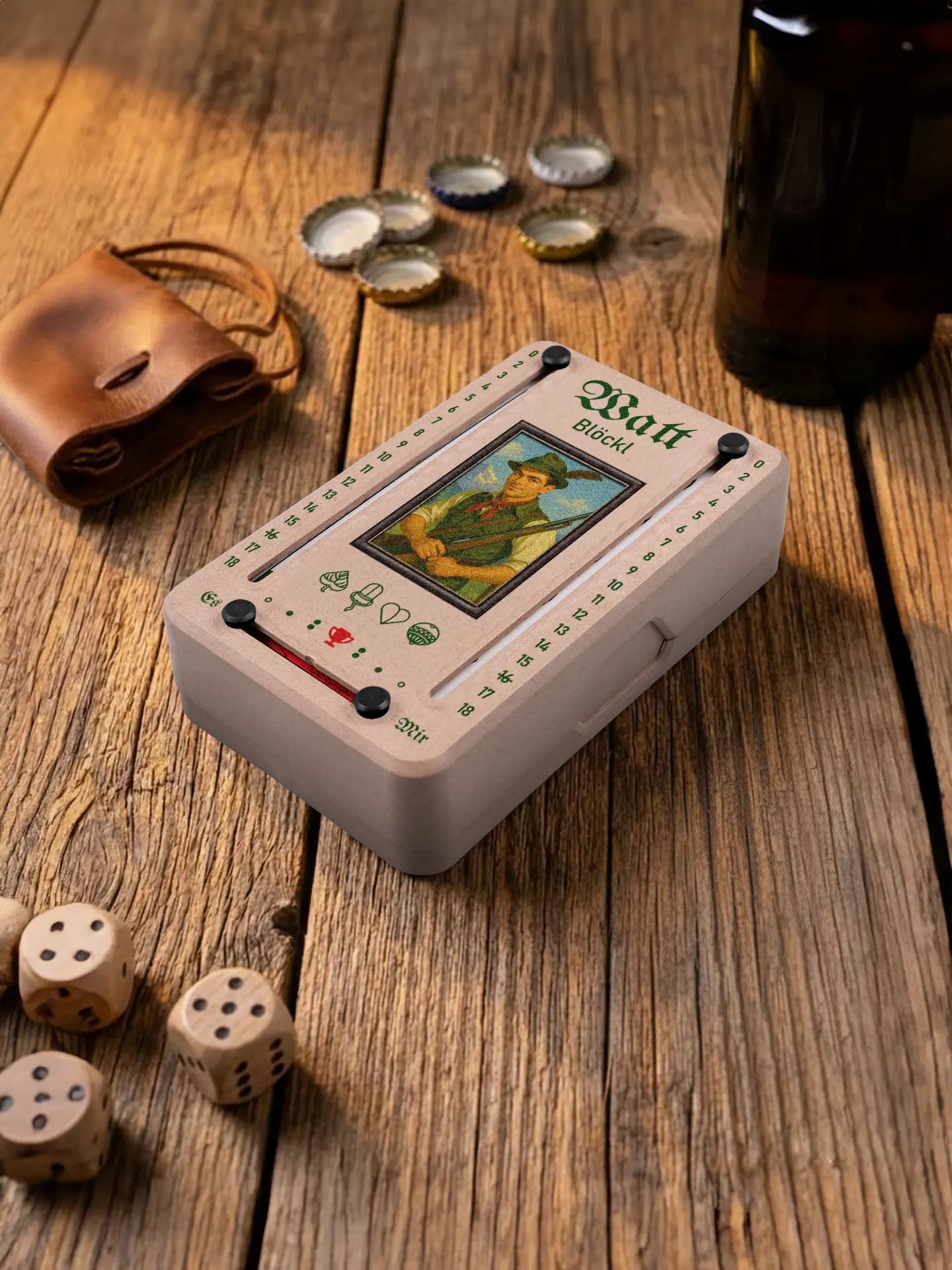 Wattblöckl in Holzoptik mit schwarzen Pins und Alpenjaeger-Motiv. Platziert auf Holztisch mit Würfeln und Kronkorken.