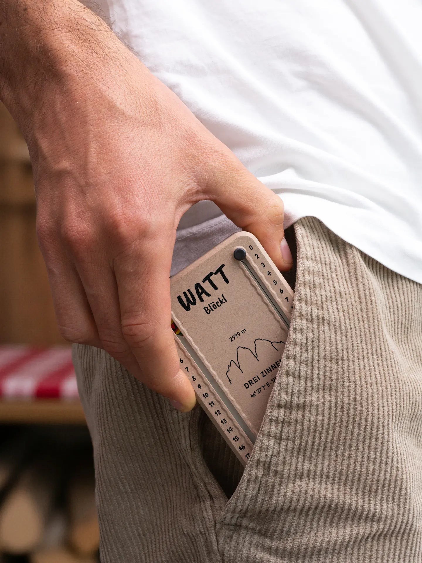 Wattblöckl in Holzoptik mit schwarzen Pins und DreiZinnen-Motiv wird aus der Hosentasche gezogen.