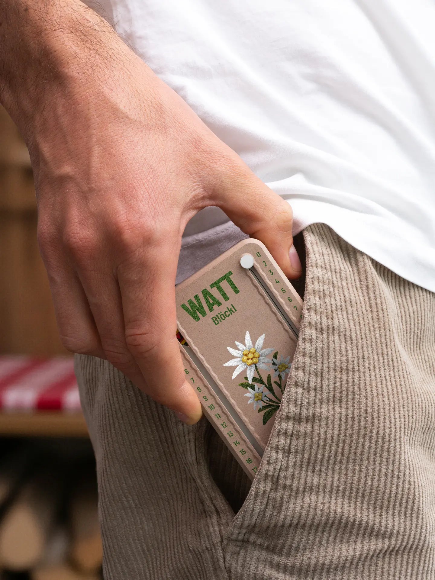 Wattblöckl in Holzoptik mit weissen Pins und Edelweiss-Motiv wird aus der Hosentasche gezogen.