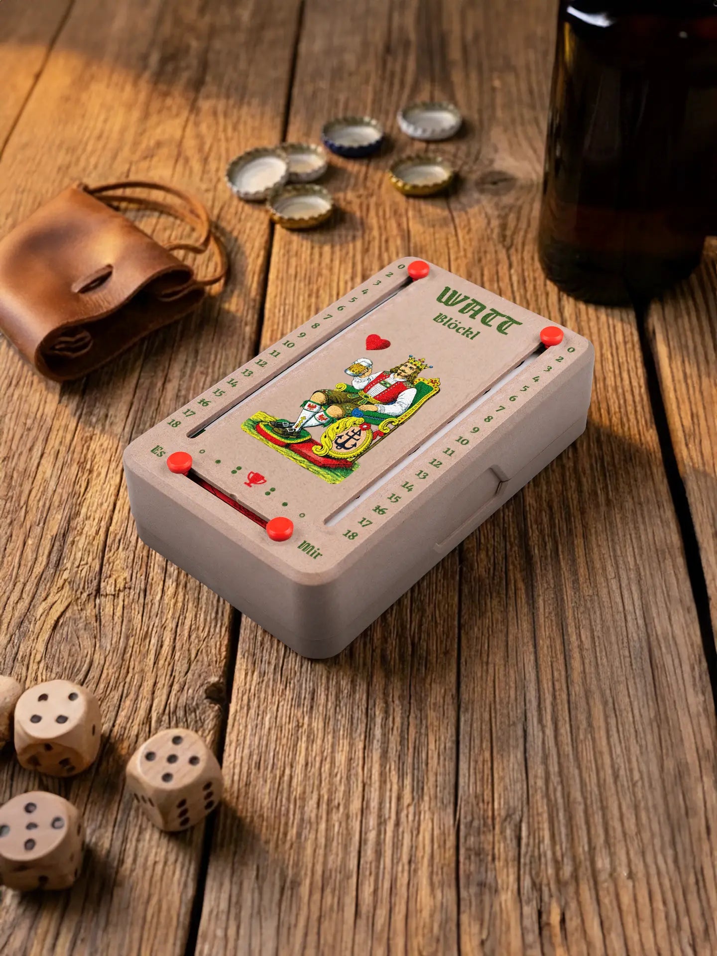 Wattblöckl in Holzoptik mit roten Pins und HerzKoenig-Motiv. Platziert auf Holztisch mit Würfeln und Kronkorken.