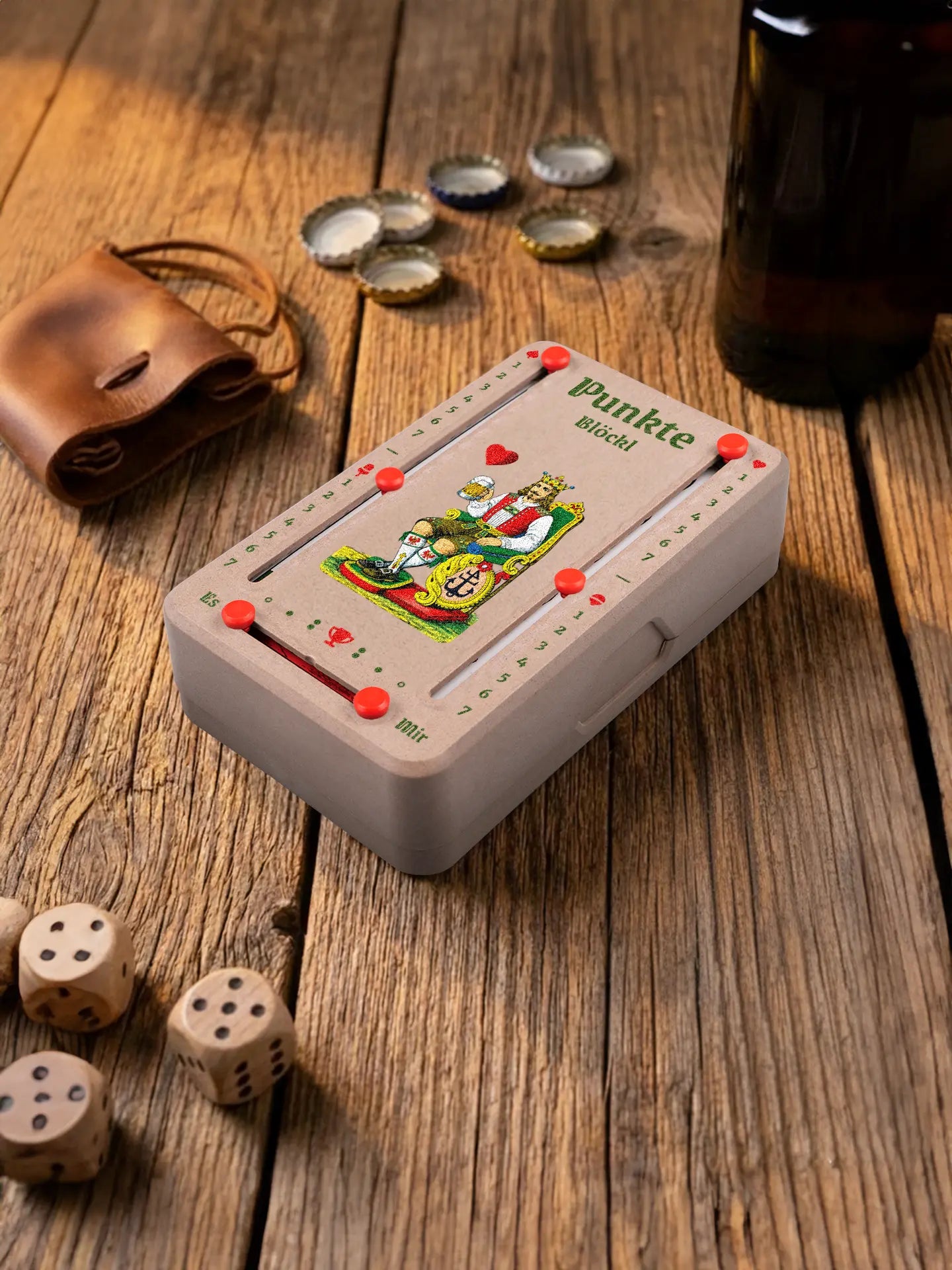 Punkteblöckl in Holzoptik mit roten Pins und HerzKoenig-Motiv. Platziert auf Holztisch mit Würfeln und Kronkorken.