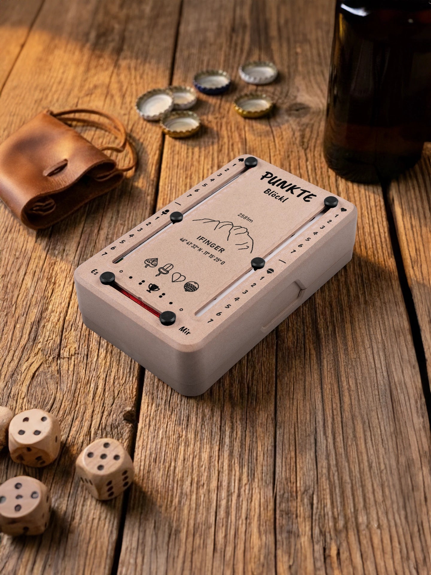 Punkteblöckl in Holzoptik mit schwarzen Pins und Ifinger-Motiv. Platziert auf Holztisch mit Würfeln und Kronkorken.
