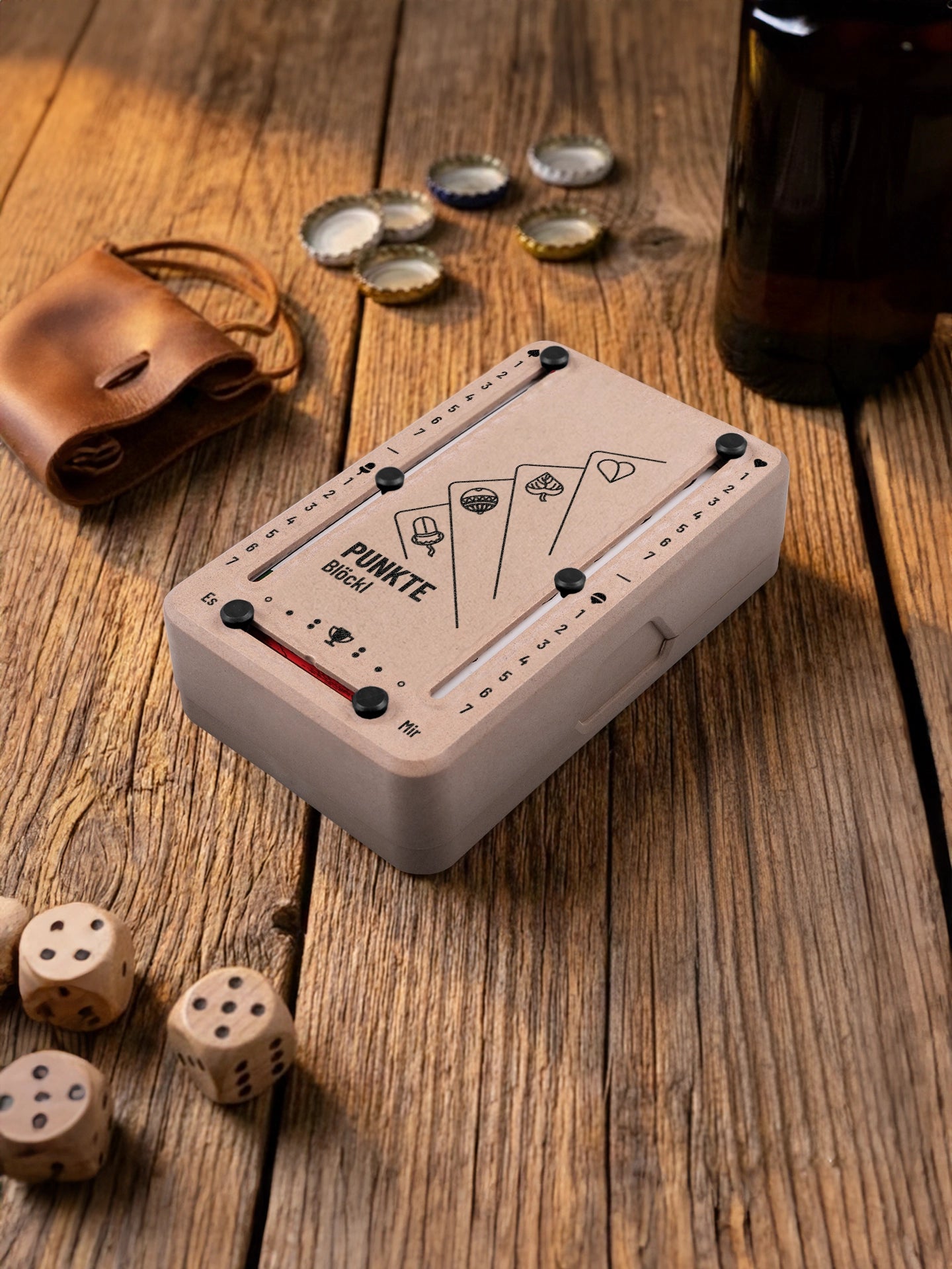 Punkteblöckl in Holzoptik mit schwarzen Pins und Karten-Motiv. Platziert auf Holztisch mit Würfeln und Kronkorken.
