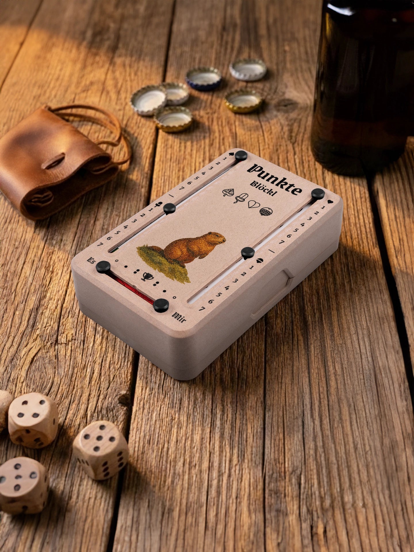 Punkteblöckl in Holzoptik mit schwarzen Pins und Murmeltier-Motiv. Platziert auf Holztisch mit Würfeln und Kronkorken.