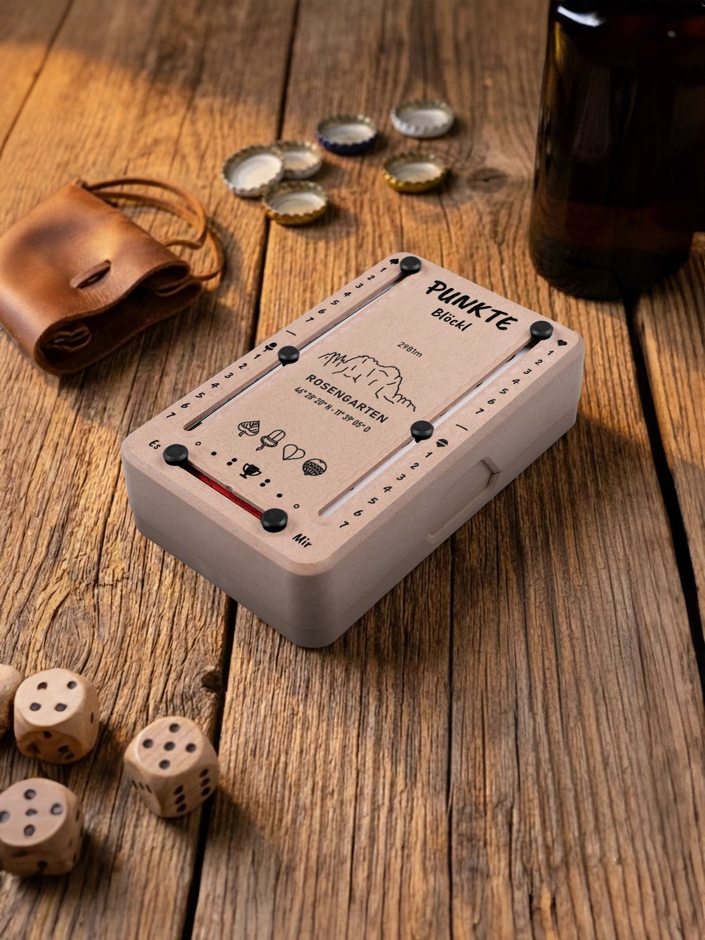 Punkteblöckl in Holzoptik mit schwarzen Pins und Rosengarten-Motiv. Platziert auf Holztisch mit Würfeln und Kronkorken.